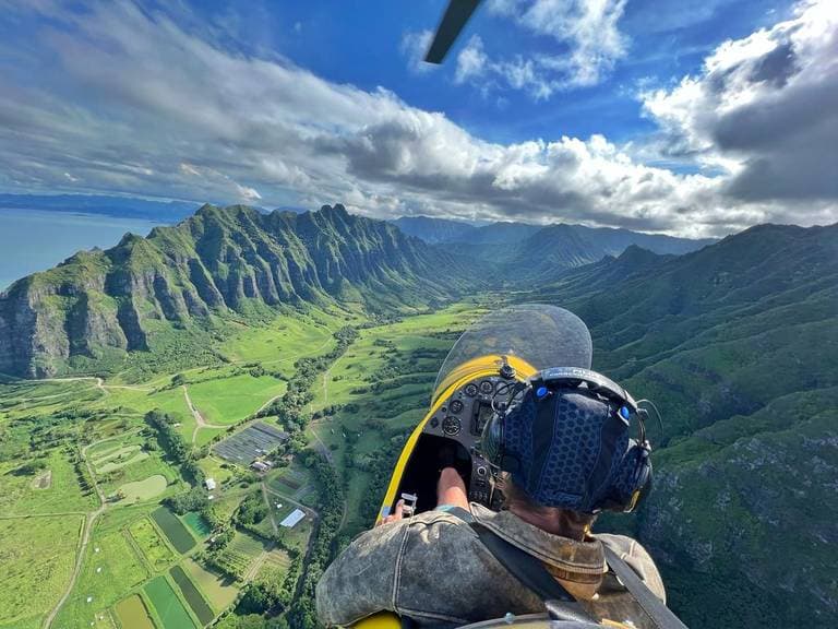 View from the rear seat of a gyroplane cockpit flying toward green Oahu mountains