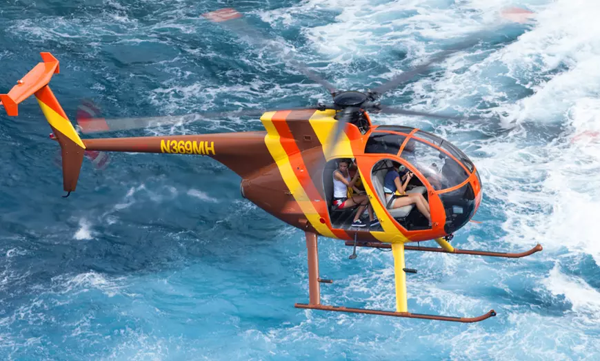 Doors-off helicopter flying low over ocean waves off Oahu